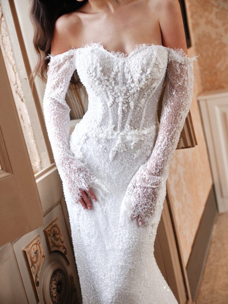 Un Abbraccio wedding dress close-up showing sweetheart neckline, fitted embellished bodice, and sheer beaded off-the-shoulder sleeves