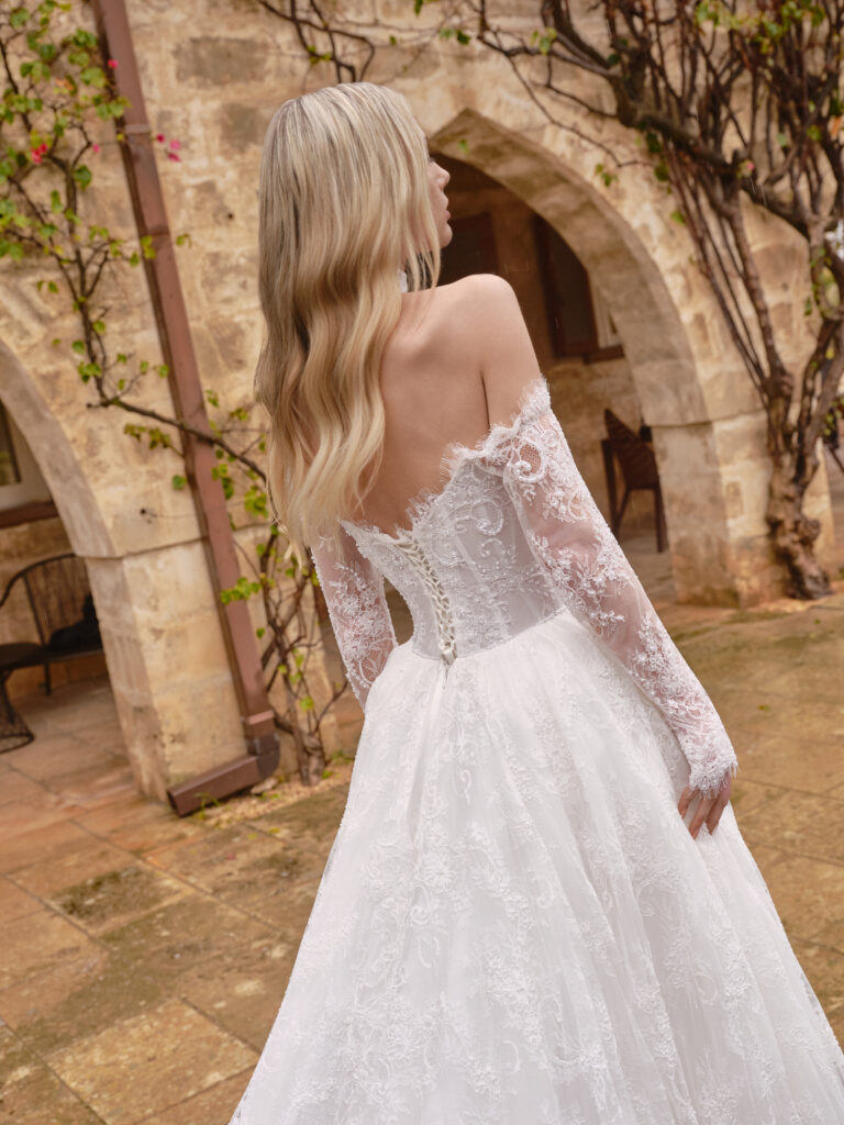 Stella Mia bridal gown angled back view showing off-the-shoulder lace sleeves and full lace skirt